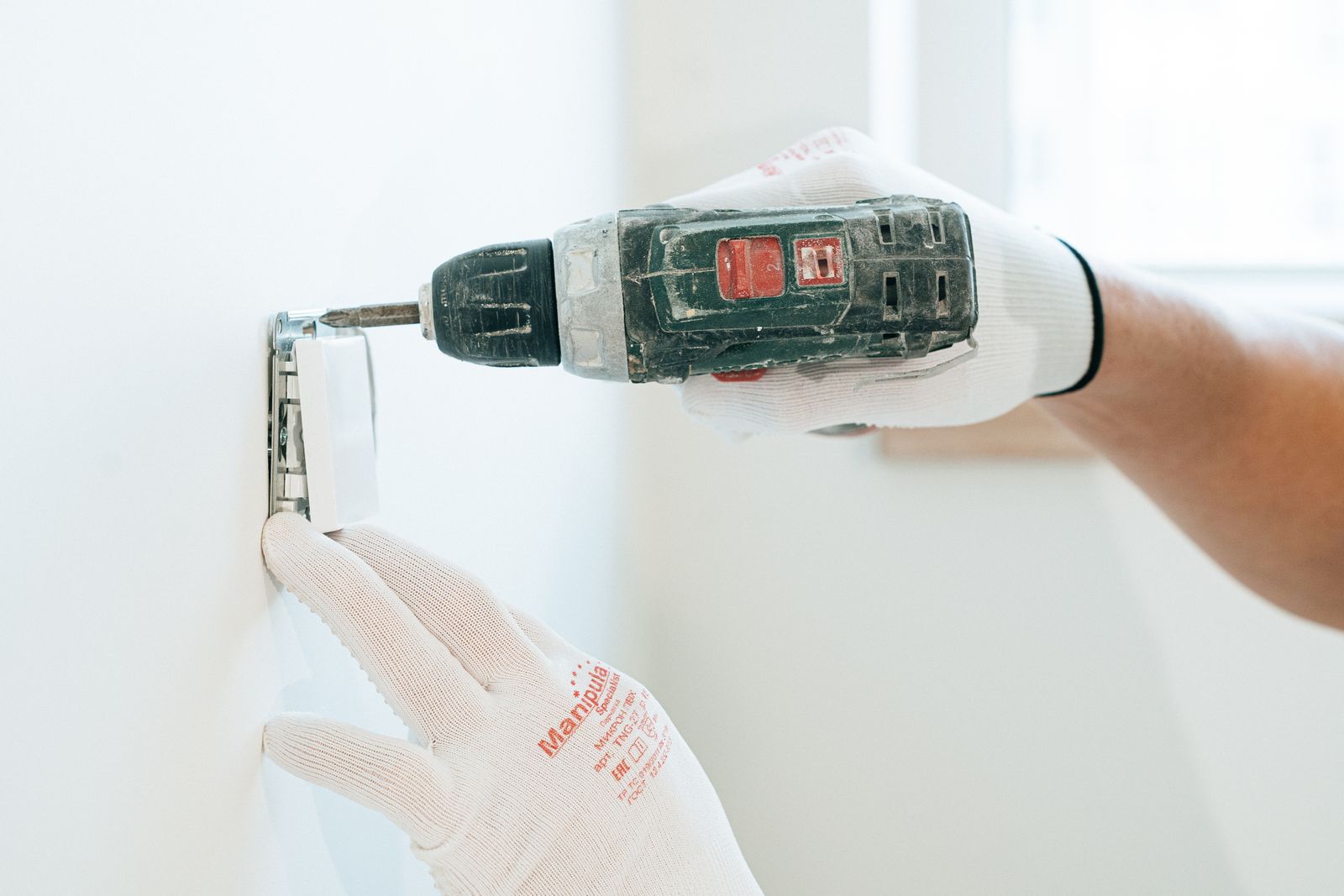 Mains gantées qui percent un mur pour fixer un boîtier