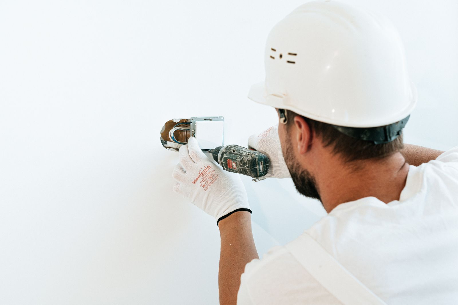 Ouvrier qui visse au mur avec une perceuse, casque et gants